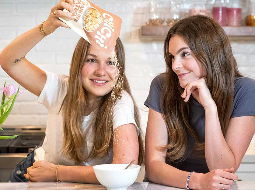 two young women at counter pouring cereal into bowl