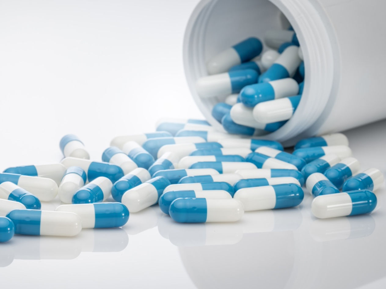 Blue-white antibiotic capsule pills spread out of plastic drug bottles.