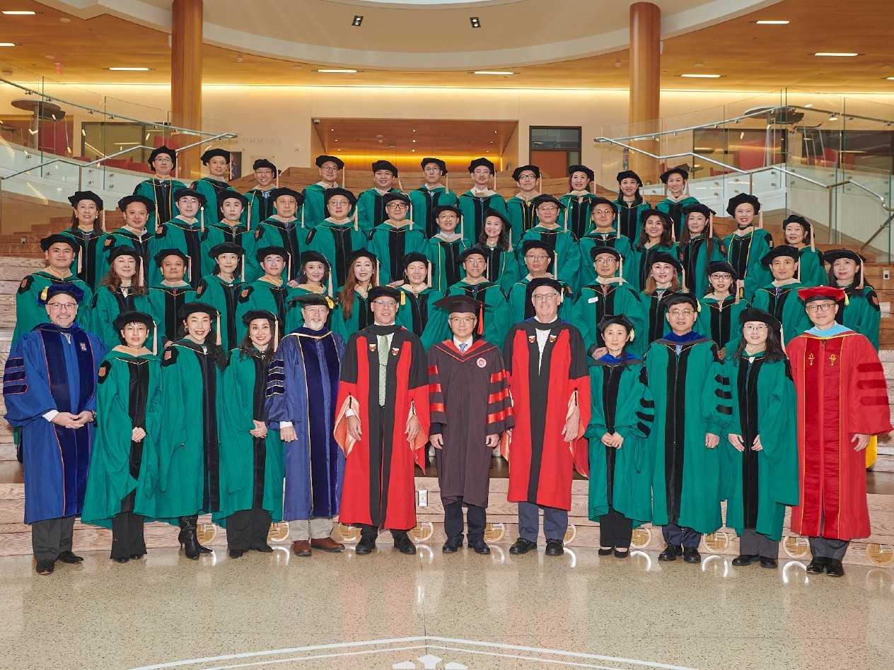 A group of people, most of them wearing green graduation robes.