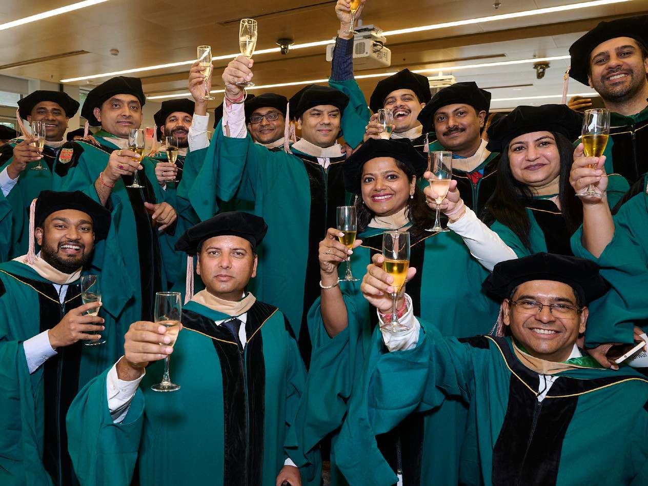 A group of people in graduation gowns toast with glasses of champagne.