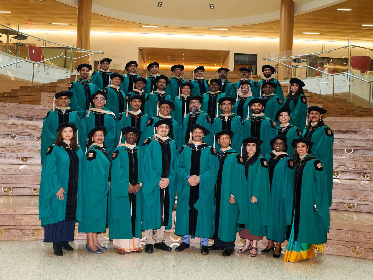 A group of graduates standing together in green graduation robes.