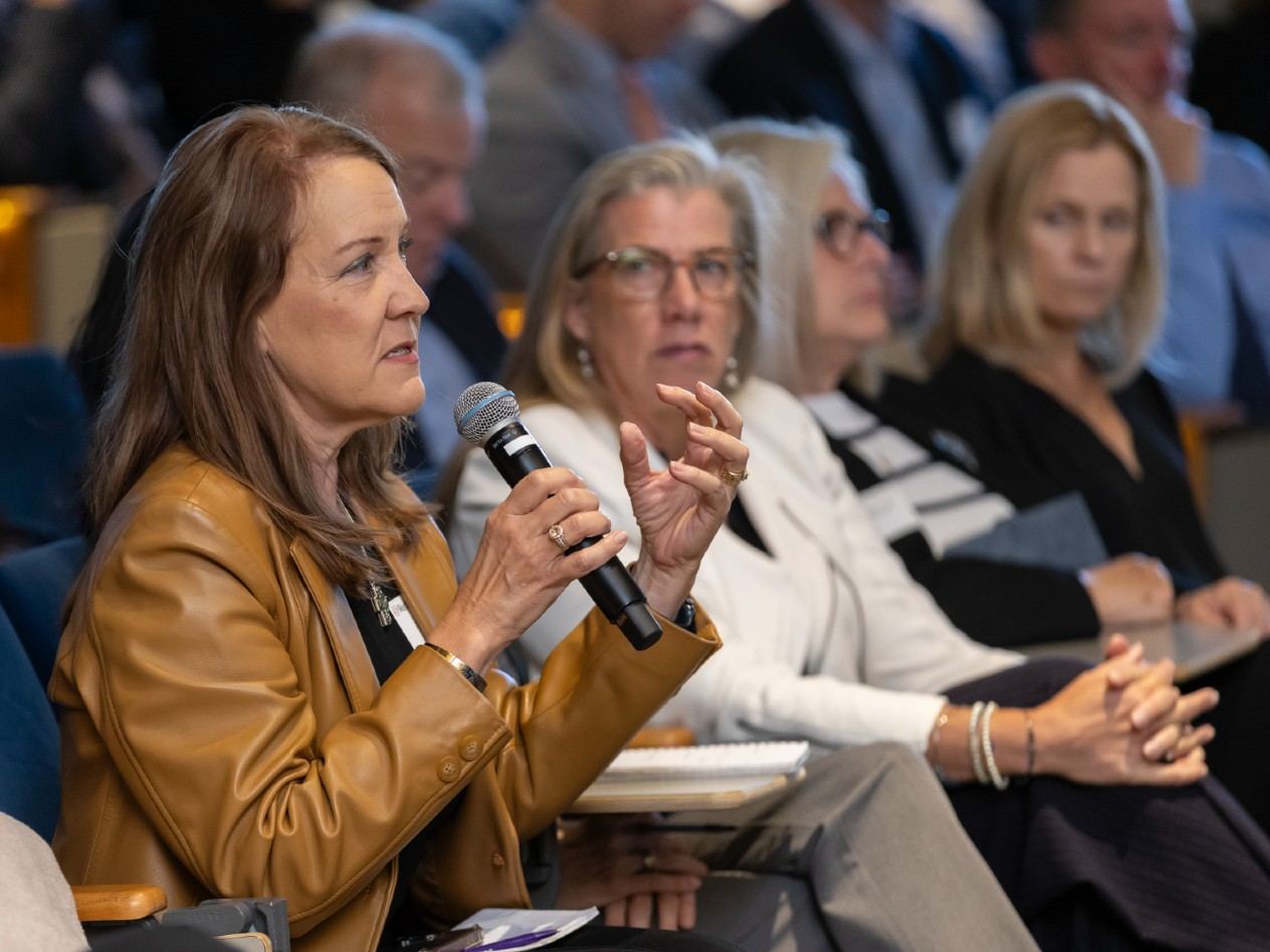 A woman seated in the audience of an auditorium speaks, holding a microphone.