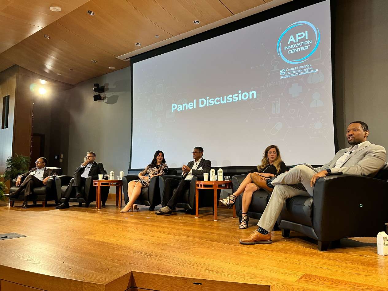 six people are seated on a stage in front of a projected image that says "panel discussion"