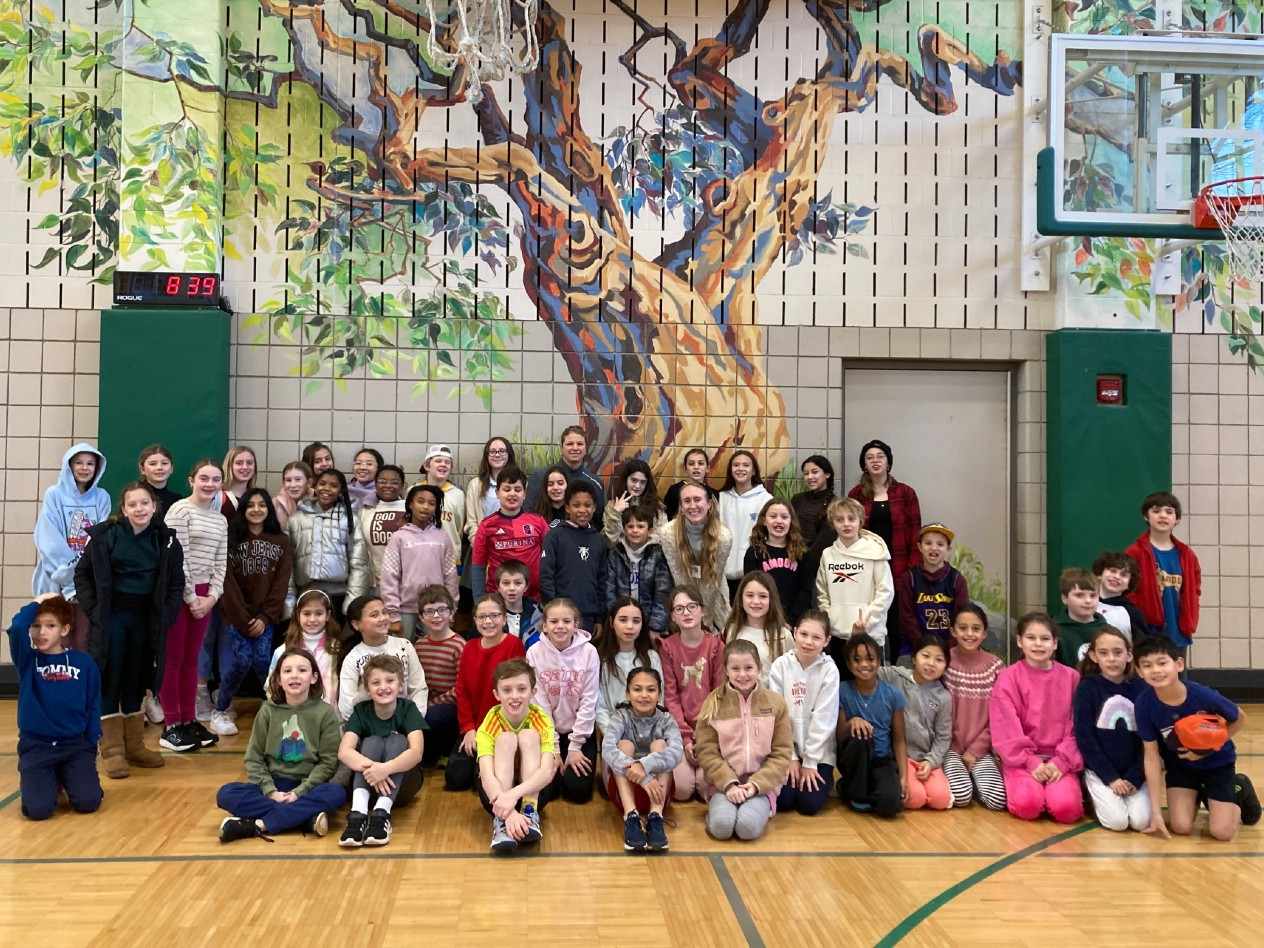 a group of young students sits in front of a mural of a tree