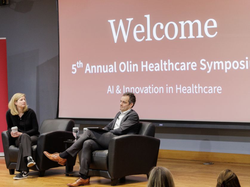 Sarah London and Peter Boumgarden seated on stage in front of a slide saying "5th annual healthcare symposium: AI and innovation in healthcare."